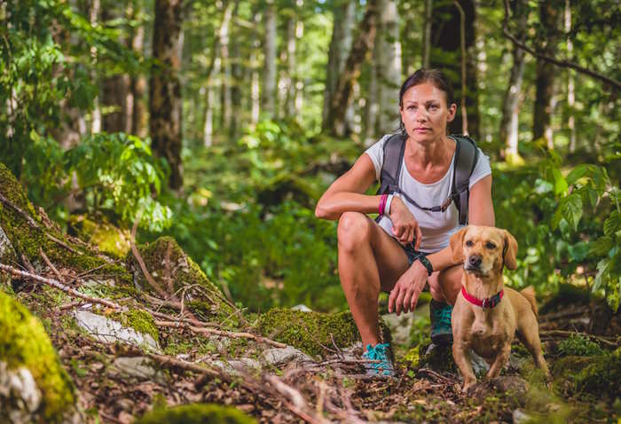 A woman with a backpack and her dog are seen on a hiking path